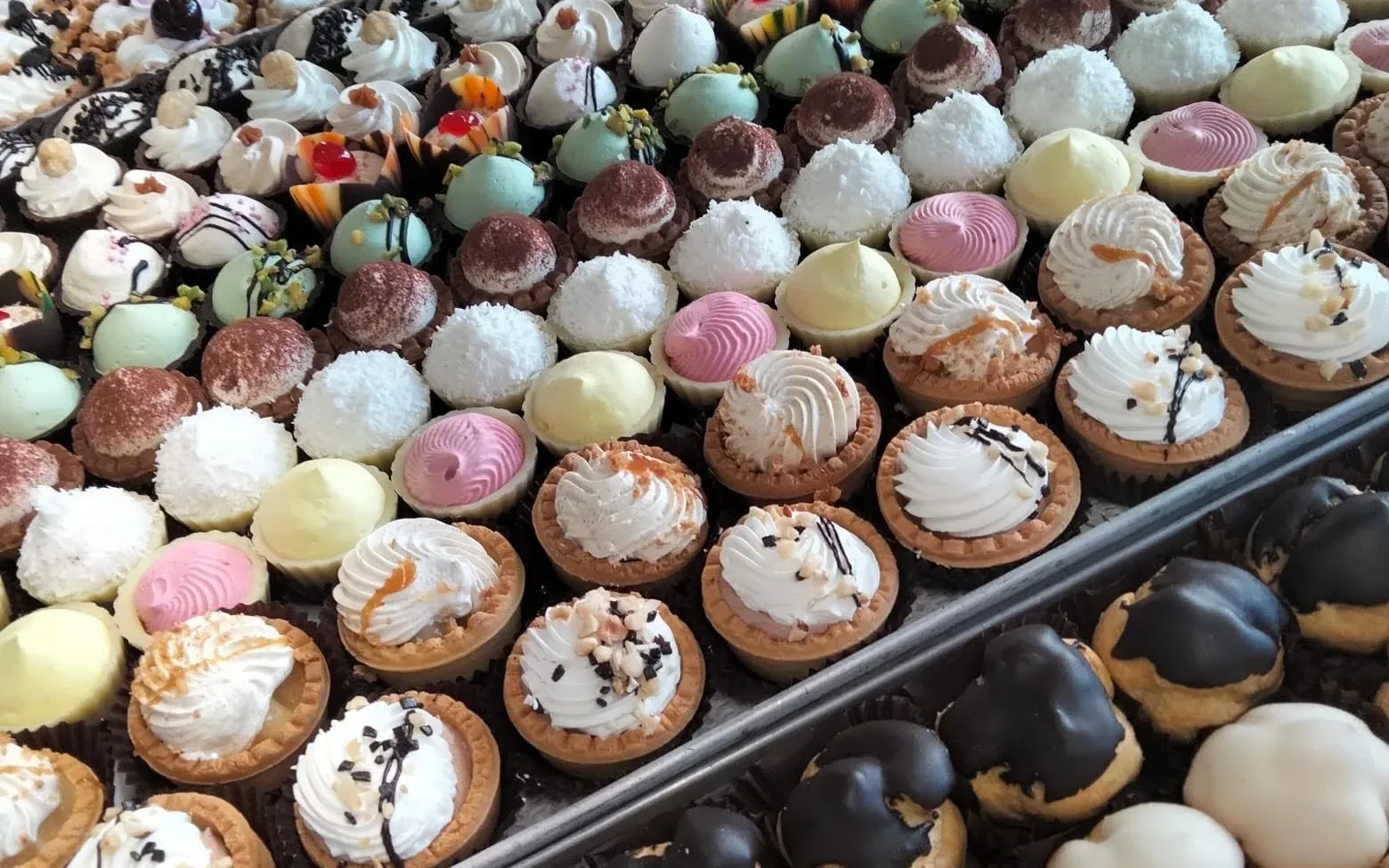Vassoi di paste mignon, tartellette e bignè nella vetrina della pasticceria