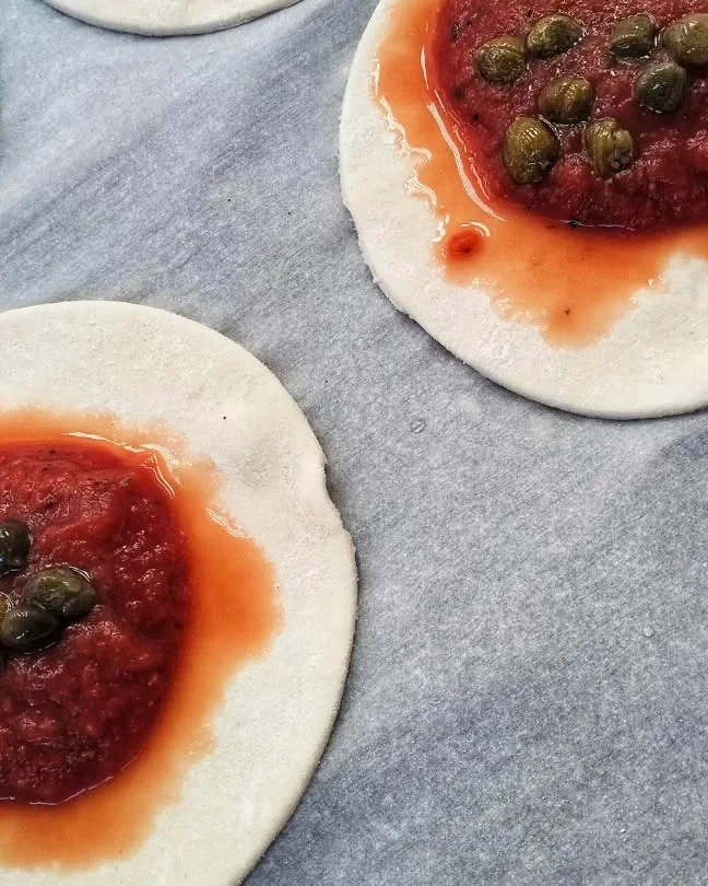 Pizzette con pomodoro e capperi pronte da infornare