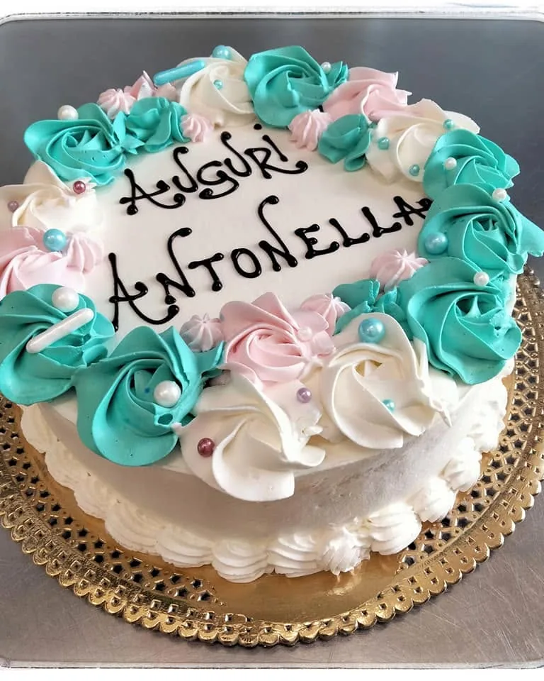 Torta di compleanno con rose turchesi e rosa e la scritta Auguri in cioccolato