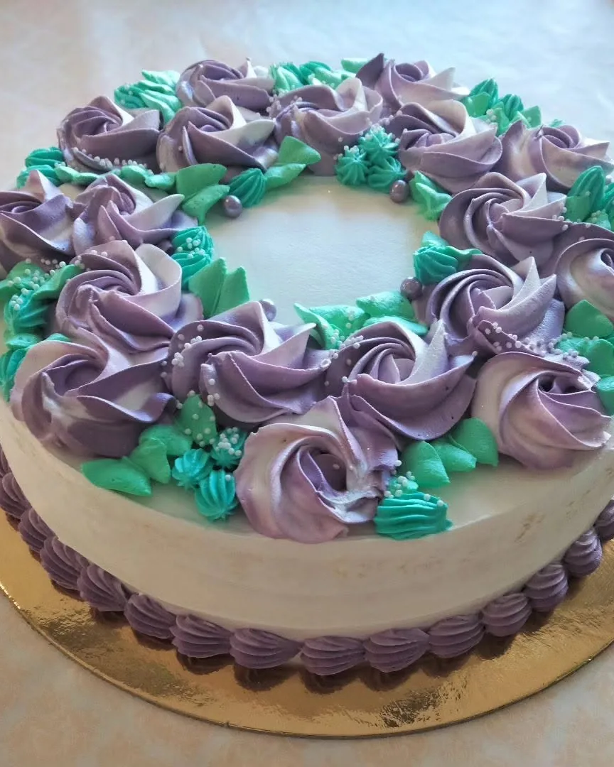 Torta con rose di panna montata lilla e foglie verdi in pasta di zucchero
